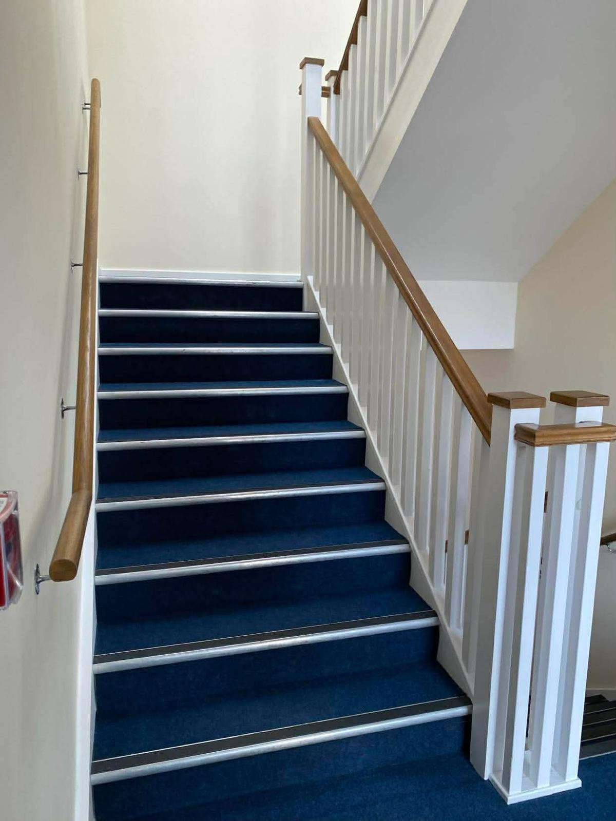 Blue carpeted staircase with white spindles and an oak handrail in the Kingston block