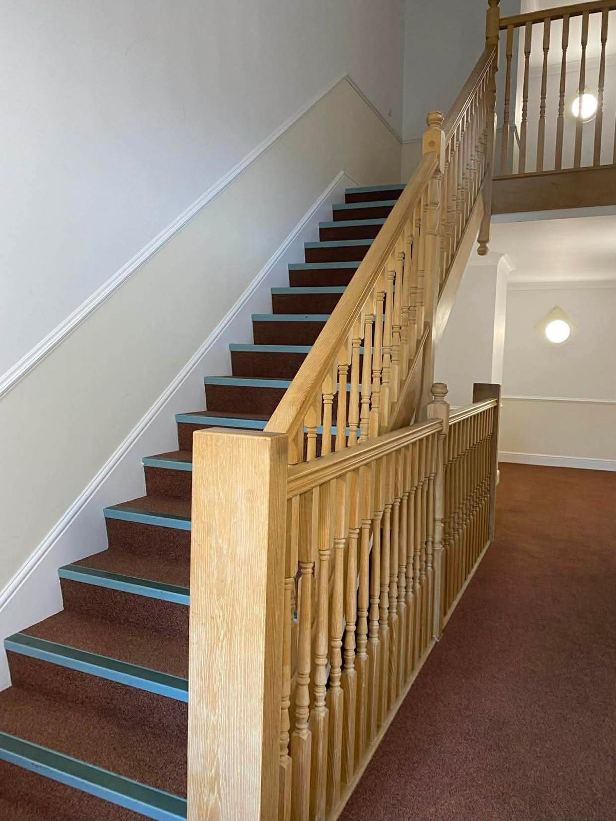 Carpeted communal staircase in the Sutton block, with a light oak balustrade and painted stair nosings