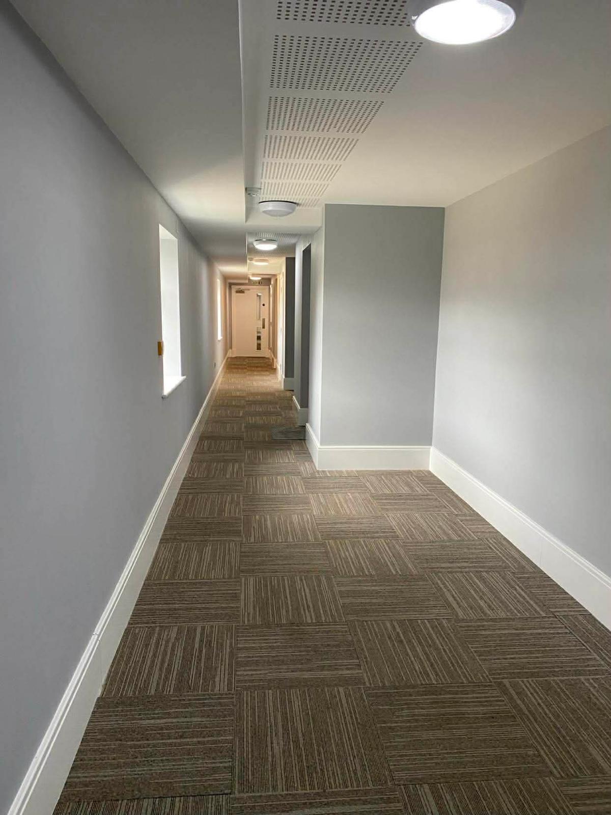 Carpet-tiled communal corridor under acoustic ceiling tiles in the second Wallington block
